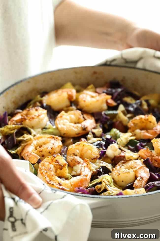 Holding a skillet with sausage and shrimp, cabbage, zucchini and mushrooms.