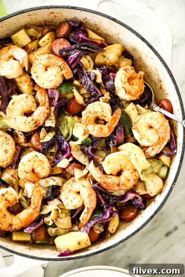 Shrimp and sausage skillet with cabbage, zucchini and mushrooms in a skillet with a serving spoon.