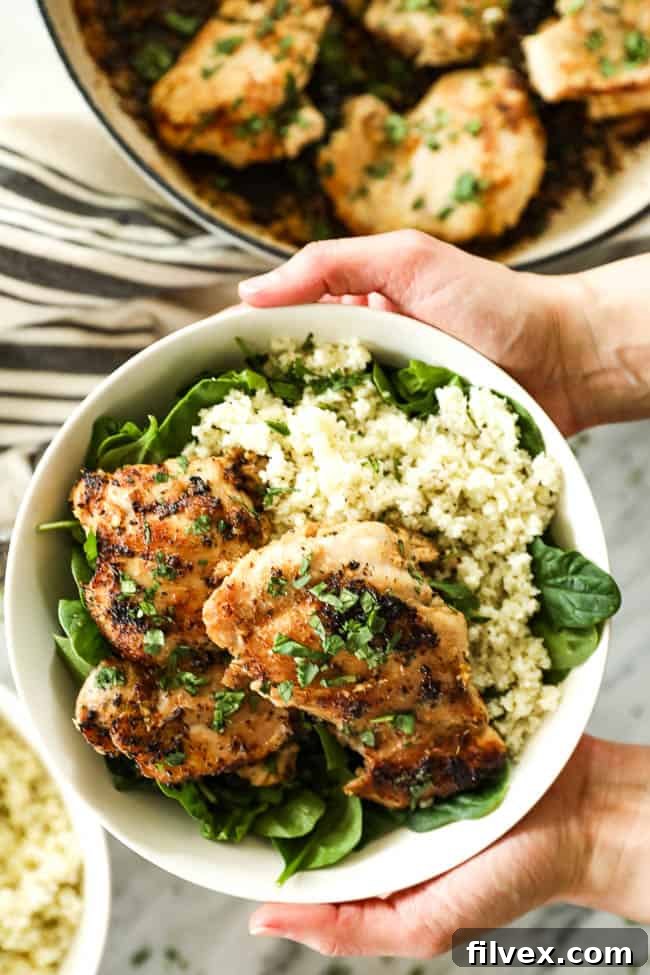 A bowl featuring a balanced meal of fresh greens, fluffy cauliflower rice, and flavorful lemongrass chicken topped with cilantro.
