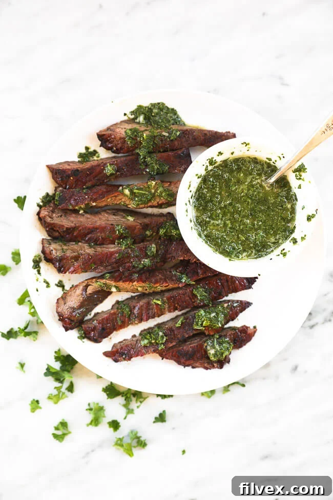 Overhead shot of sliced skirt steak on a white plate with chimichurri sauce over the steak and on the side