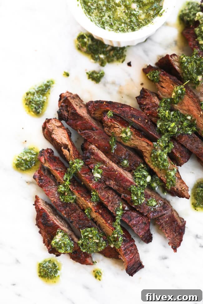 Sliced steak on marble with chimichurri sauce drizzled on top