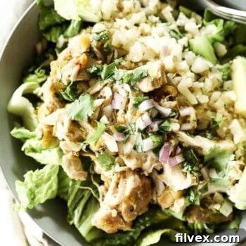 Close up of Mexican shredded chicken in a bowl with romaine lettuce, cauliflower rice and avocado. Topped chopped red onion and cilantro.