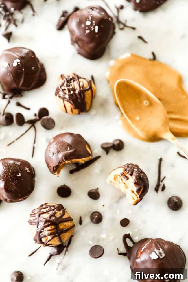 Delicious peanut butter balls, some elegantly drizzled with rich chocolate and others fully coated, artistically arranged on a marble surface and sprinkled with flaky sea salt. A spoonful of creamy peanut butter sits nearby, inviting you to indulge in these healthy, no-bake energy bites.