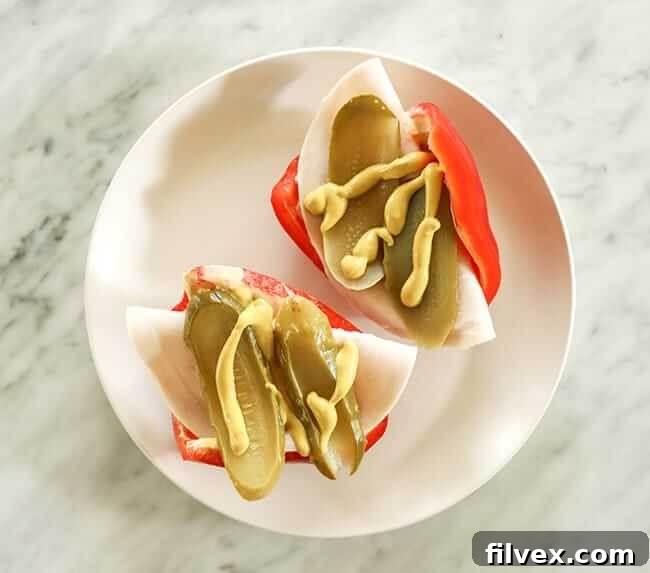 Half bell peppers topped with lunch meat, pickles and mustard on a plate