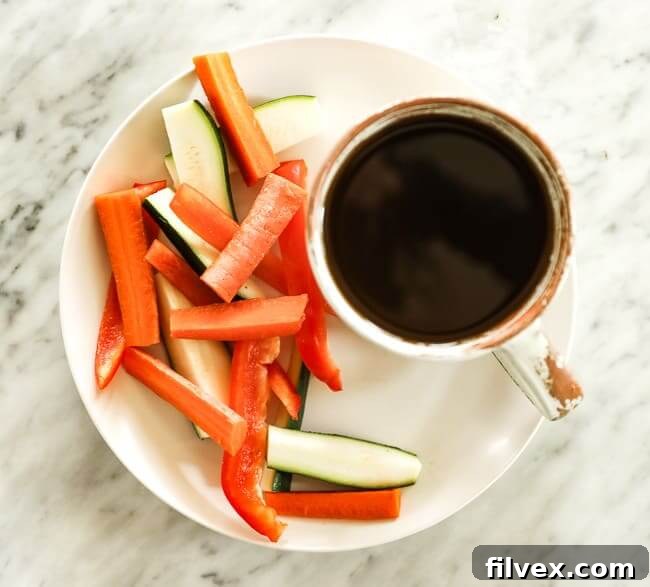 Sliced carrots, bell pepper and zucchini on a plate with a cup of broth
