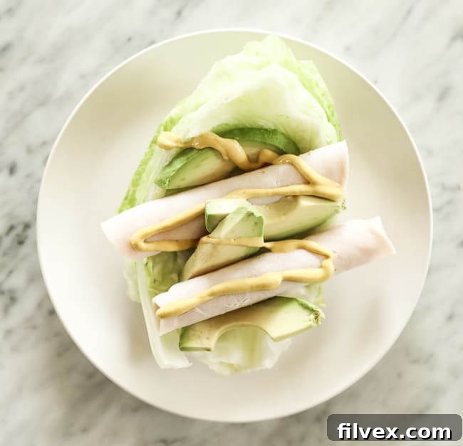 Iceburg lettuce shell topped with lunch meat, avocado and mustard on a plate