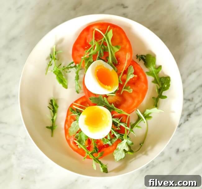 Sliced tomato topped with arugula and soft boiled egg on a plate