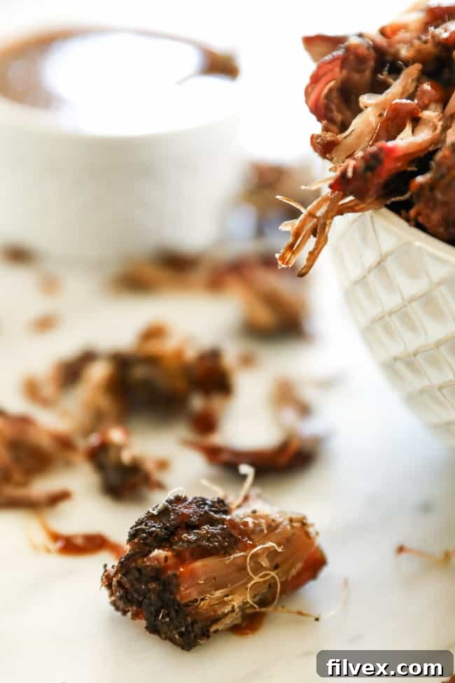 Close-up of pieces of perfectly smoked pork shoulder on a marble surface with a bowl in the background, showcasing the crispy bark and tender meat.