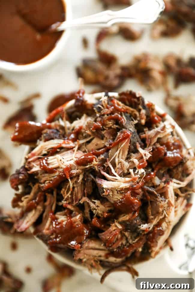 Overhead shot of smoked pork shoulder pieces in a bowl, drizzled with a rich BBQ sauce, highlighting its juicy texture.