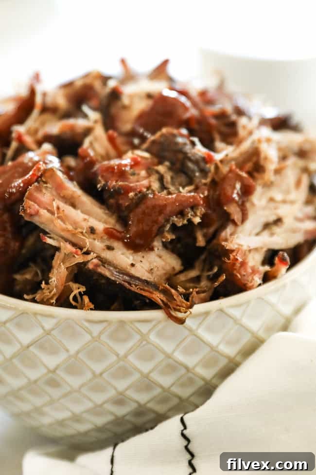 Close-up, angled shot of smoked pork shoulder pieces in a bowl, richly coated with sauce, emphasizing its delicious texture.