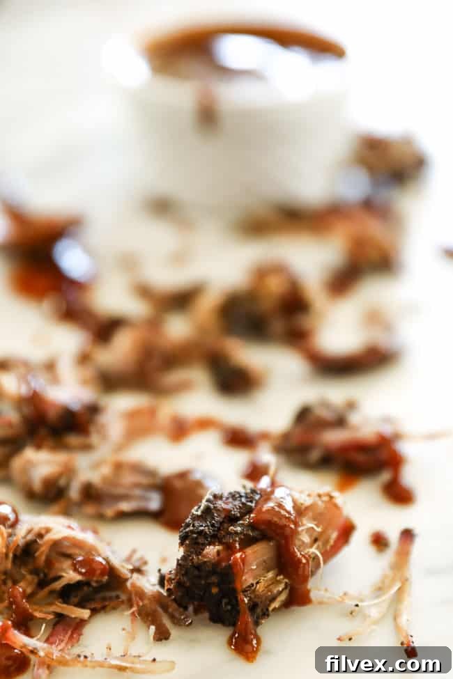 Extreme close-up of smoked pork shoulder pieces on a marble surface with sauce drizzled on top, highlighting the tender meat and flavorful bark.