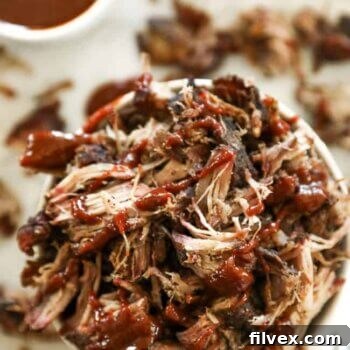 Smoked pork shoulder pieces in a bowl with sauce over the top.