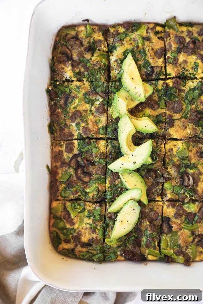 Keto breakfast casserole sliced in a dish with sliced avocado topping overhead vertical image