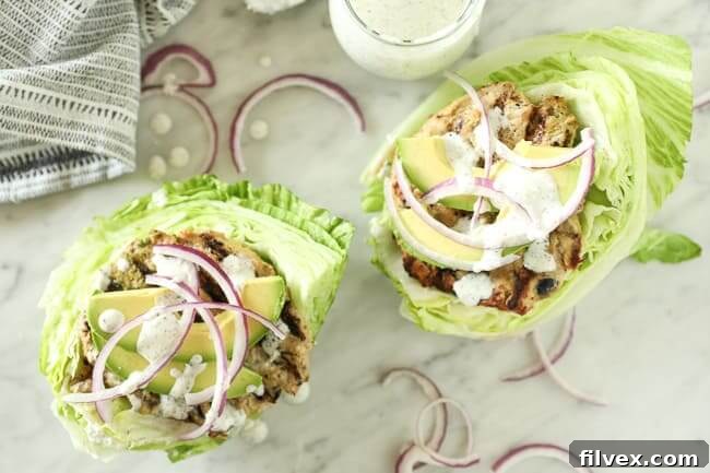 Overhead view of two Greek turkey burgers nestled on lettuce leaves, garnished with sliced avocado, red onion, and a generous drizzle of dairy-free tzatziki sauce. The vibrant colors highlight the freshness of the ingredients.