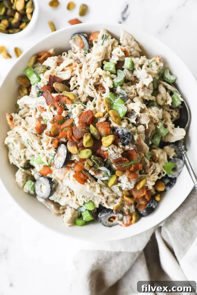 Vertical overhead image of chicken salad in a bowl with a spoon in it and extra bacon on the side, highlighting its deliciousness.