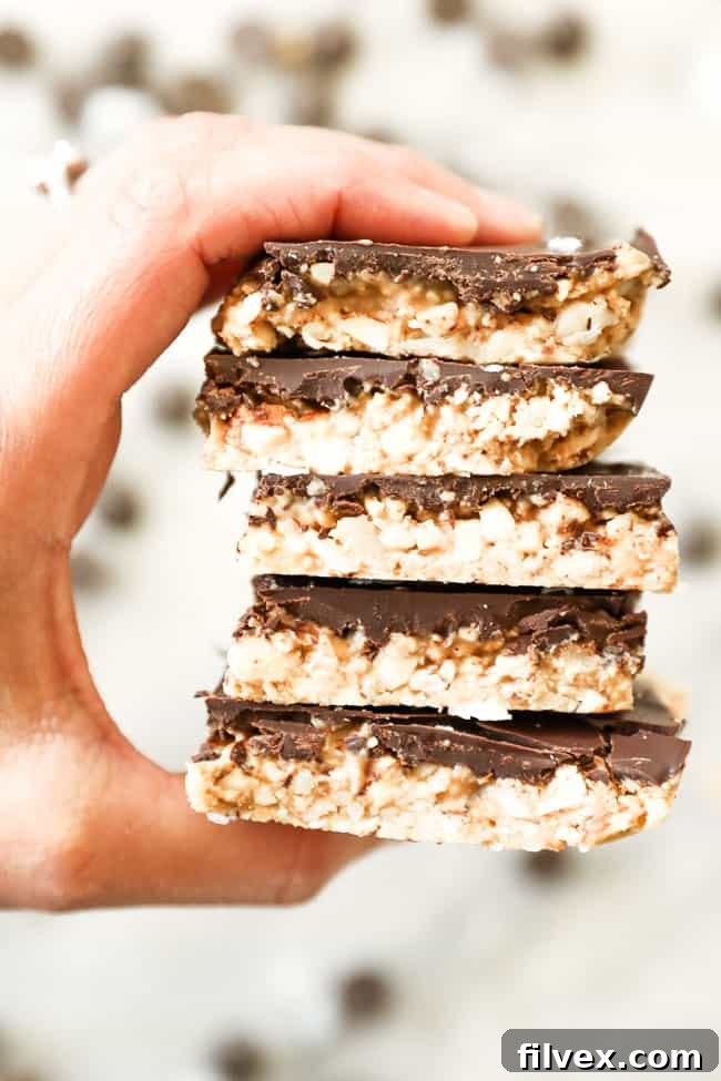 A person's hand gracefully holding a stack of three perfectly portioned, delicious no-bake peanut butter bars, showcasing their appealing thickness and homemade charm against a soft, blurred background.