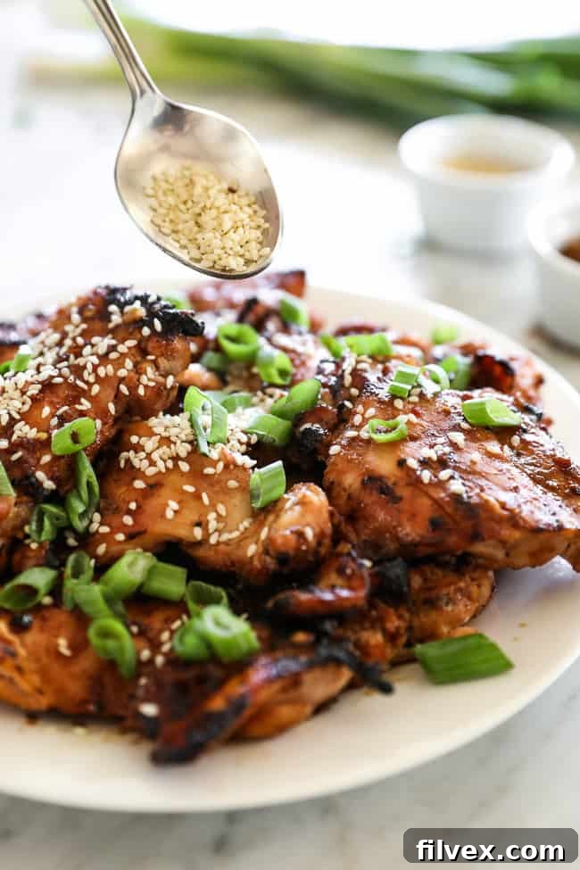Korean BBQ chicken stacked on a plate with spoon of sesame seeds coming in.