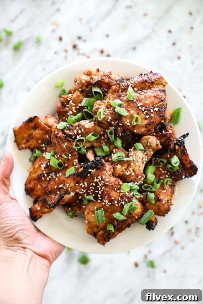 Hand holding up Korean BBQ chicken on a plate with green onion slices.