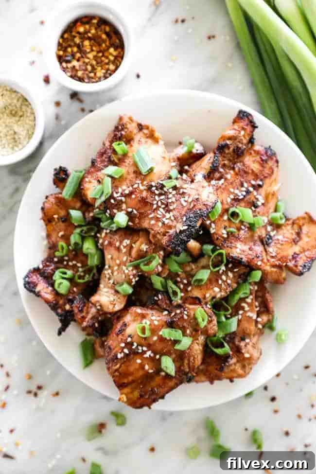 Overhead shot of korean bbq chicken stacked on a plate with sliced green onions on top