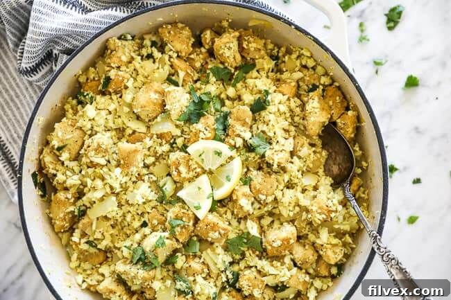 Flavorful Indian chicken and cauliflower rice in a pan, garnished with cilantro and lemon slices, ready to be served.