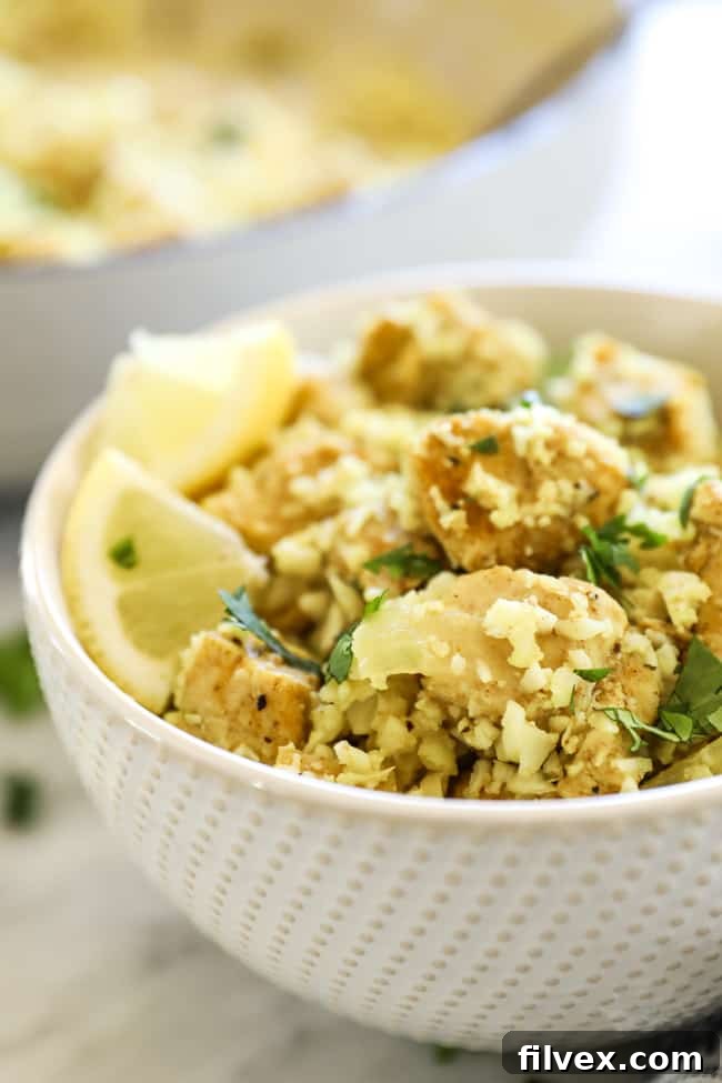 Close-up view of a bowl of Indian chicken with cauliflower rice, garnished with fresh lemon wedges, highlighting its vibrant colors and textures.