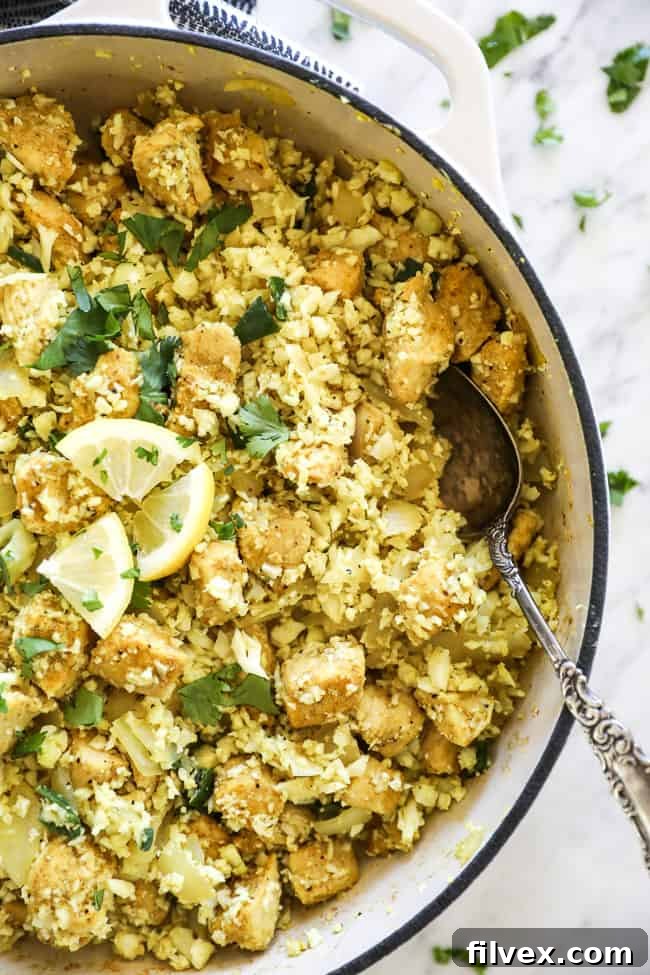 Overhead shot of Indian chicken and cauliflower rice in a pan, with a serving spoon on the side, showcasing the simplicity of this one-pan meal.
