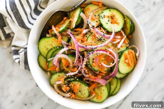 Asian cucumber salad in a bowl with spoon. Red onion and sesame seeds on top