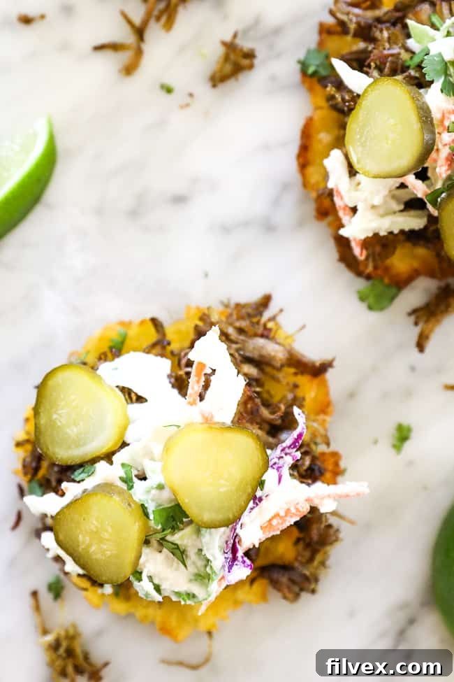 Overhead image of smashed plantain bun with pulled pork, slaw and pickles on top. 