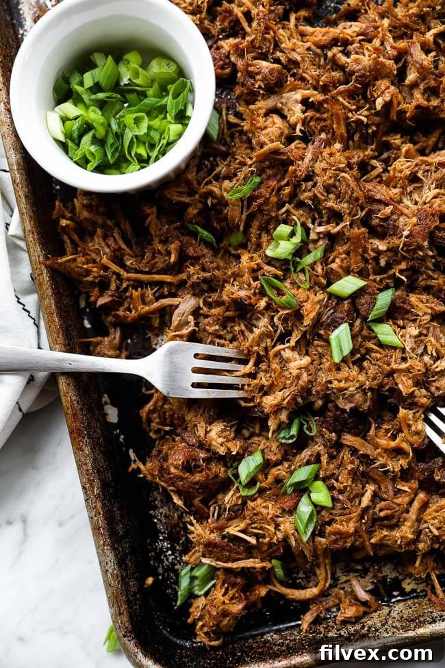 Easy slow cooker pulled pork on sheet pan with two forks and sliced green onions vertical image