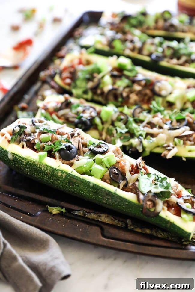 Angled vertical image of zucchini pizza boats on sheet pan. Loaded with marinara sauce, italian sausage, bell pepper, mushrooms, olives and cheese. Fresh basil sprinkled on top.
