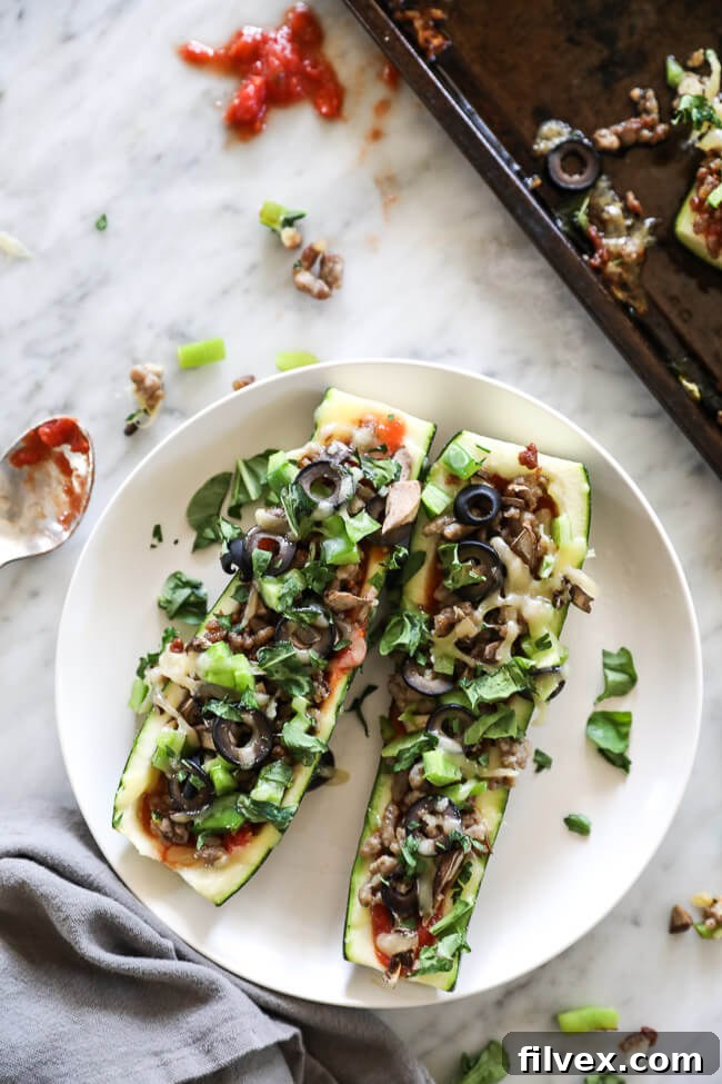 Overhead vertical image of zucchini pizza boats on sheet pan. Loaded with marinara sauce, italian sausage, bell pepper, mushrooms, olives and cheese. Fresh basil sprinkled on top.