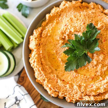 Easy cauliflower hummus in a rustic bowl with fresh chopped vegetables like carrots, celery, and cucumber arranged neatly on the side.