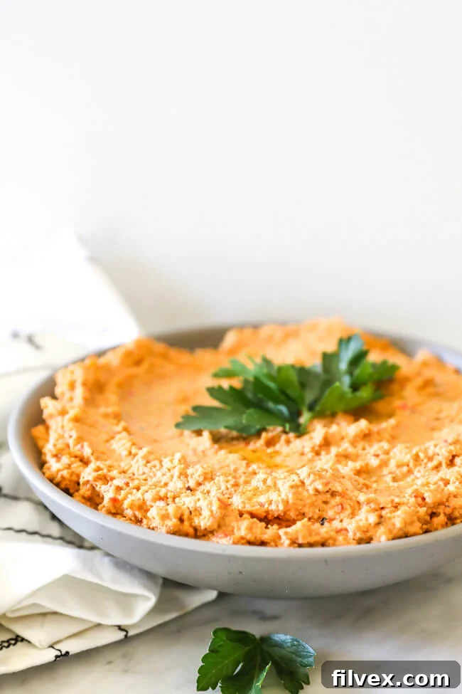 Close-up vertical shot of easy cauliflower hummus in a bowl, garnished with fresh chopped parsley on top, viewed from an angle to show its texture and vibrant color.