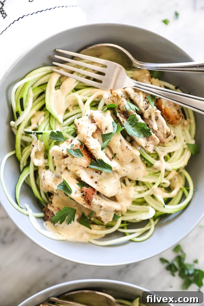 Overhead vertical image close up of creamy chicken alfredo in a bowl with a fork and spoon. 
