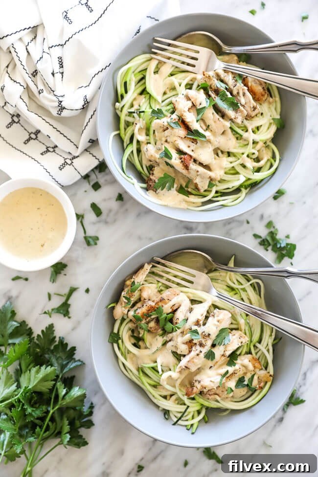 Overhead vertical image of two bowls of creamy chicken alfredo with a fork and spoon in each bowl. Extra sauce on the side with chopped parsley spread about. 