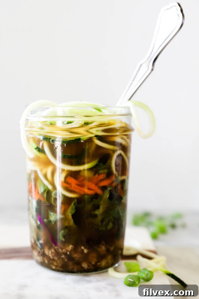 Straight on vertical image of healthy ramen noodles in a jar with broth poured in and a spoon. 