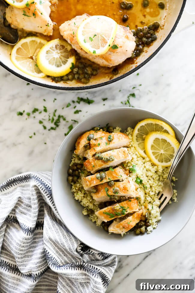 Vertical overhead image of tender Lemon Chicken Piccata, expertly sliced and served in a bowl, garnished with vibrant lemon rounds and fresh chopped parsley. A fork is poised, inviting a taste of this wholesome dish. This image highlights the dish's appetizing presentation.