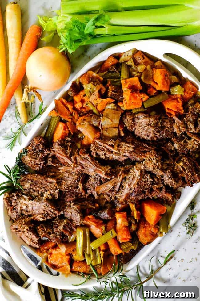 Shredded pot roast on a platter with sweet potatoes, celery and onion, a classic and hearty meal.