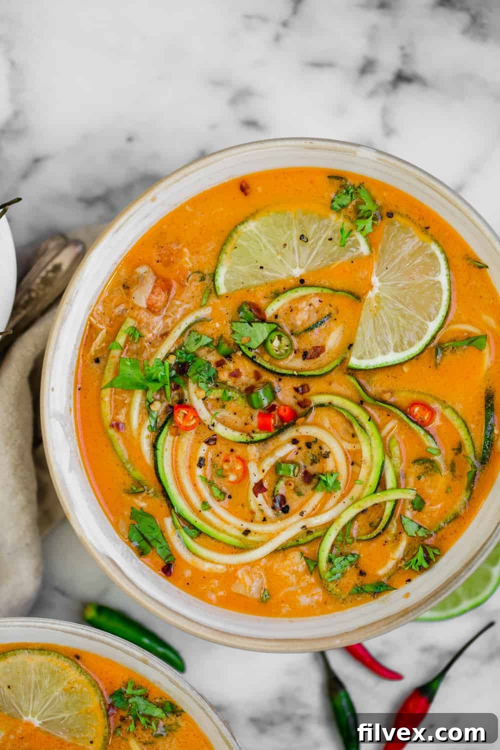 Bowl of Thai chicken soup with zoodles, limes and chopped parsley, highlighting fresh ingredients.