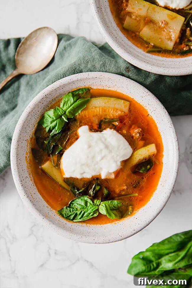Paleo lasagna soup in a bowl with basil and a dollop of dairy-free cheese, photographed from overhead.