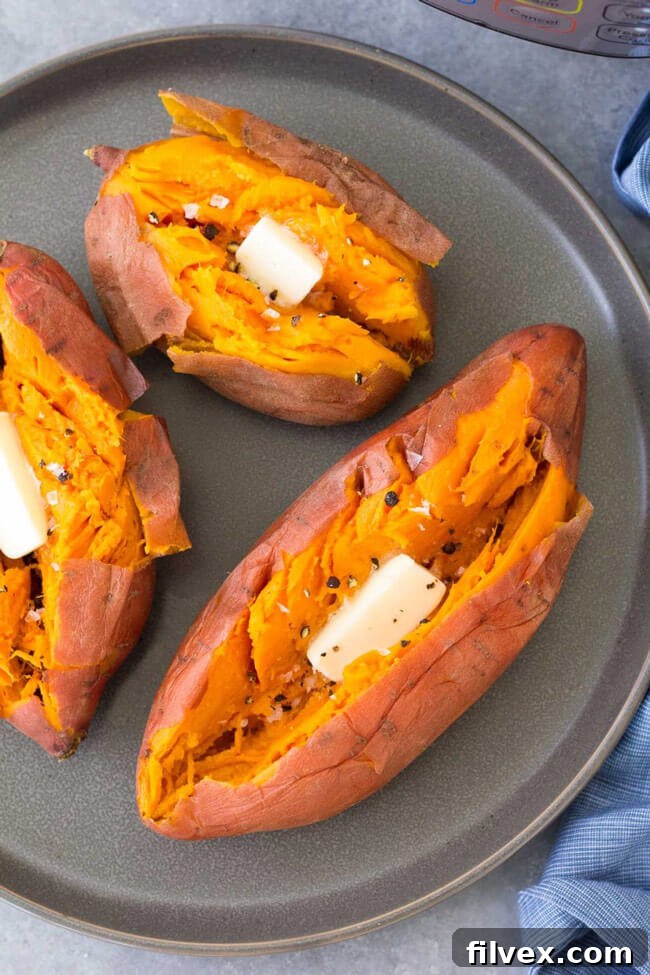 Three perfectly cooked sweet potatoes with butter in each, arranged on a plate.