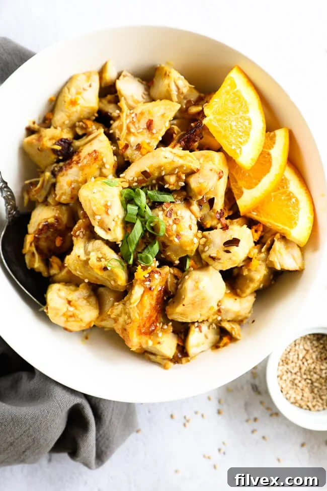 Chunks of Instant Pot orange chicken in a bowl with fresh orange wedges, highlighting its vibrant flavor.