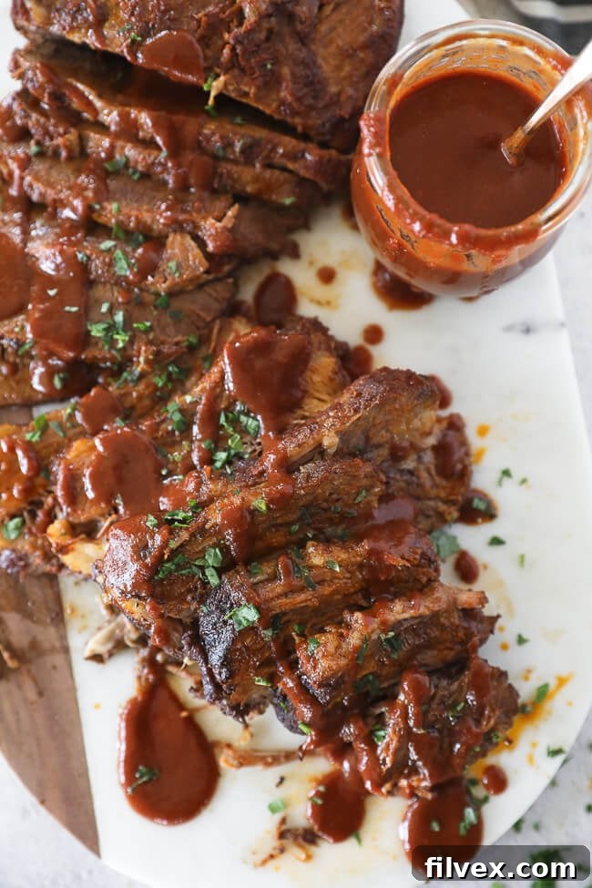 Sliced BBQ beef brisket on a platter with BBQ sauce drizzled over it, ready to be served.
