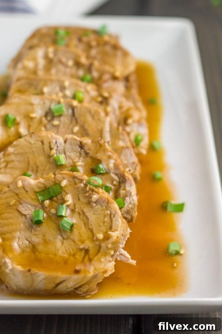 Instant Pot teriyaki pork tenderloin on a plate, stacked in a row with sauce, presented at an angle.