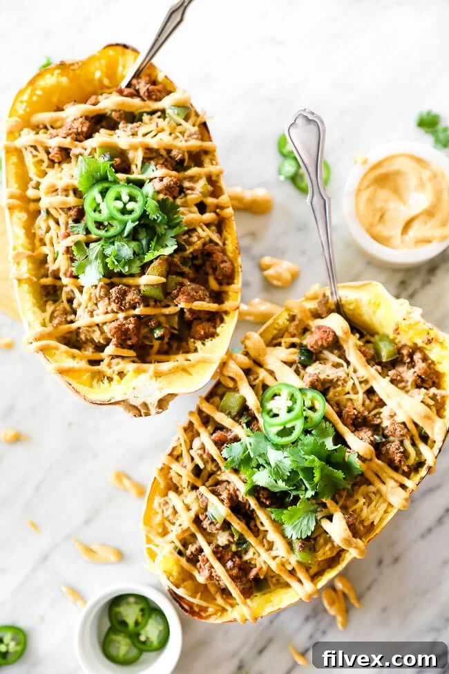 Two taco stuffed spaghetti squash with sauce drizzled on top and spoons coming out of the squash, highlighting presentation.