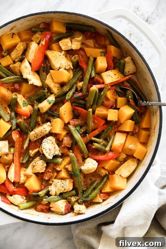 Overhead vertical image of butternut squash curry in a skillet with a serving spoon. 
