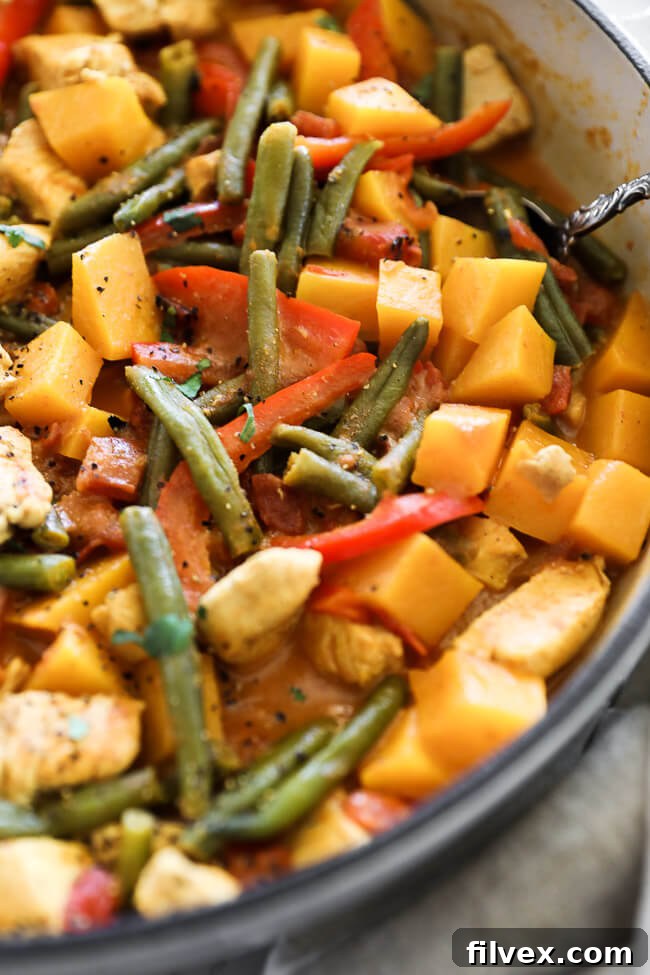 Angled vertical image of butternut squash curry in a skillet with a serving spoon. 