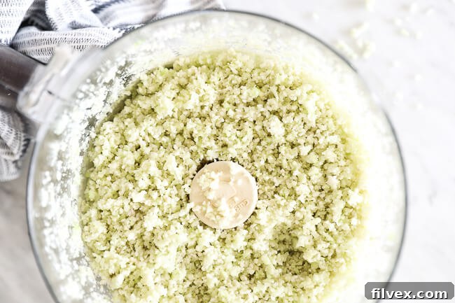 Horizontal overhead image of cauliflower rice in a food processor, emphasizing the texture and preparation.