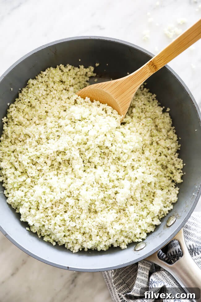 Vertical overhead image of pan-fried cauliflower rice in a skillet with a serving spoon, showcasing its golden-brown texture.