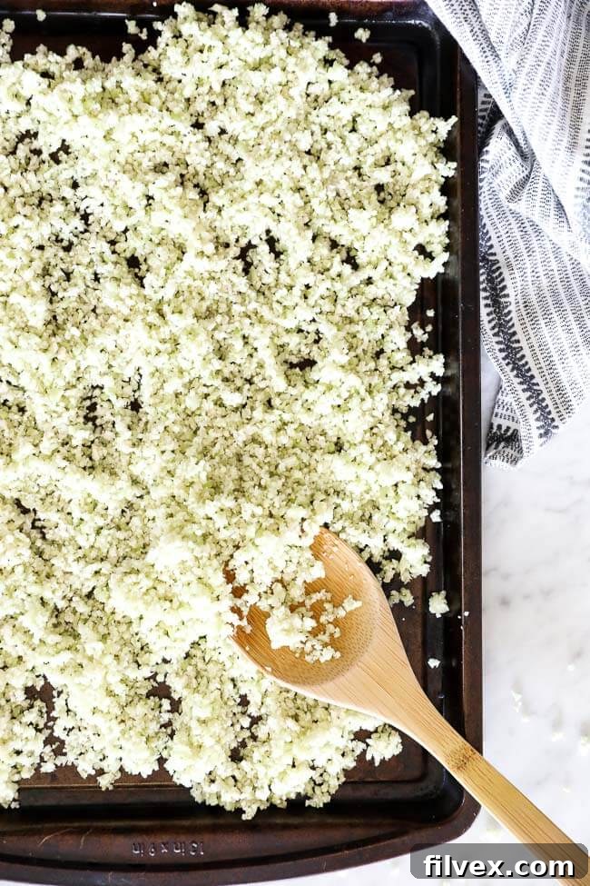 Vertical overhead image of cauliflower rice evenly spread on a sheet pan, ready for roasting.